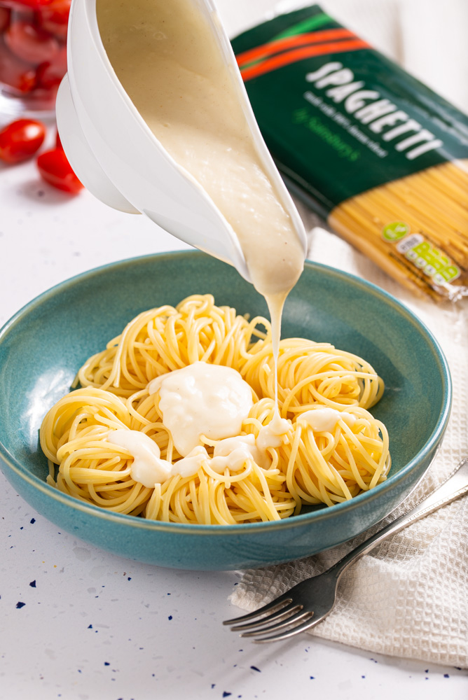 pouring bechamel sauce over bowl with spaghetti pasta