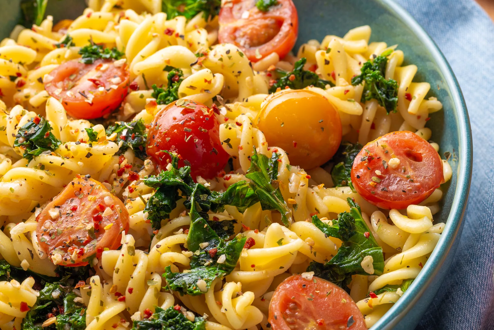 top view of half bowl filled with cherry tomatoes and kale pasta