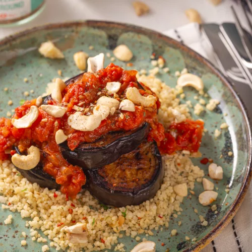 front image of a plate with eggplant topped with tomato juice on a bed of couscous