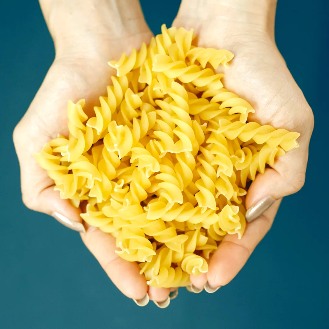 dried fusilli pasta being held with two hands
